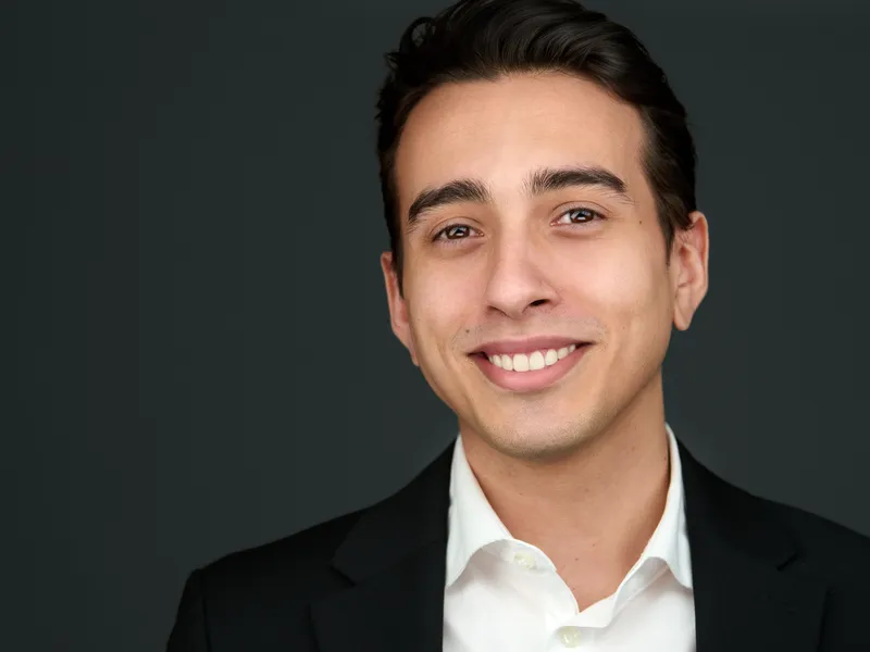 Professional headshot with confident expression, smart business attire on dark background