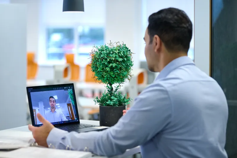Ben Rahmani seated at a laptop during a video call in a bright office setting