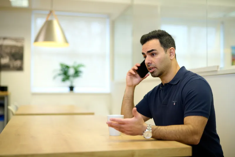 Ben Rahmani speaking on the phone with coffee in hand in a bright communal space