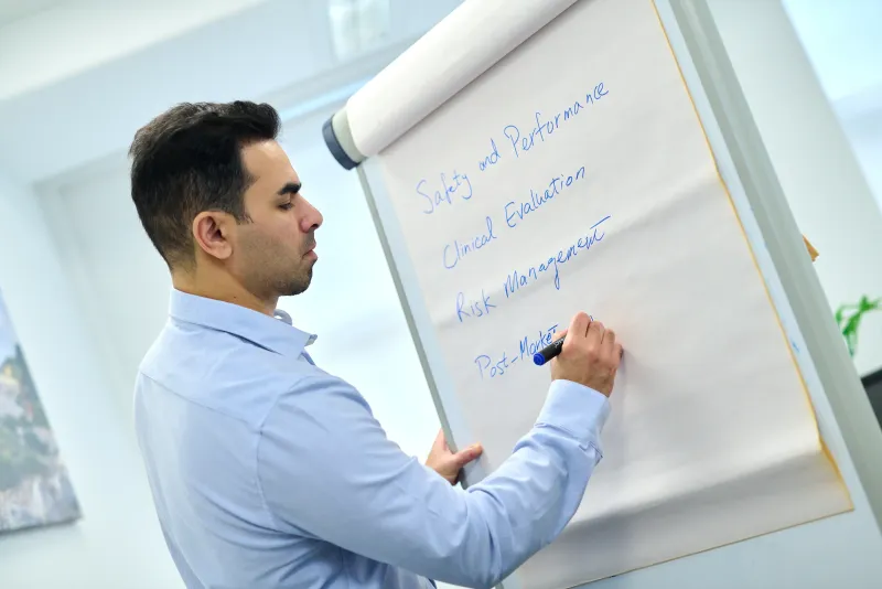 Ben Rahmani writing regulatory and clinical notes on a flipchart in a bright office setting