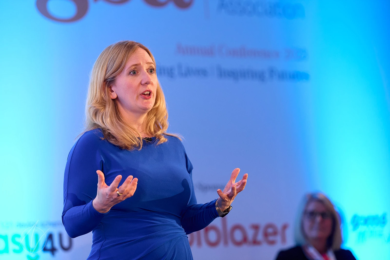 Helen Thomas presenting at the ASCL annual conference, with blue stage lighting behind her