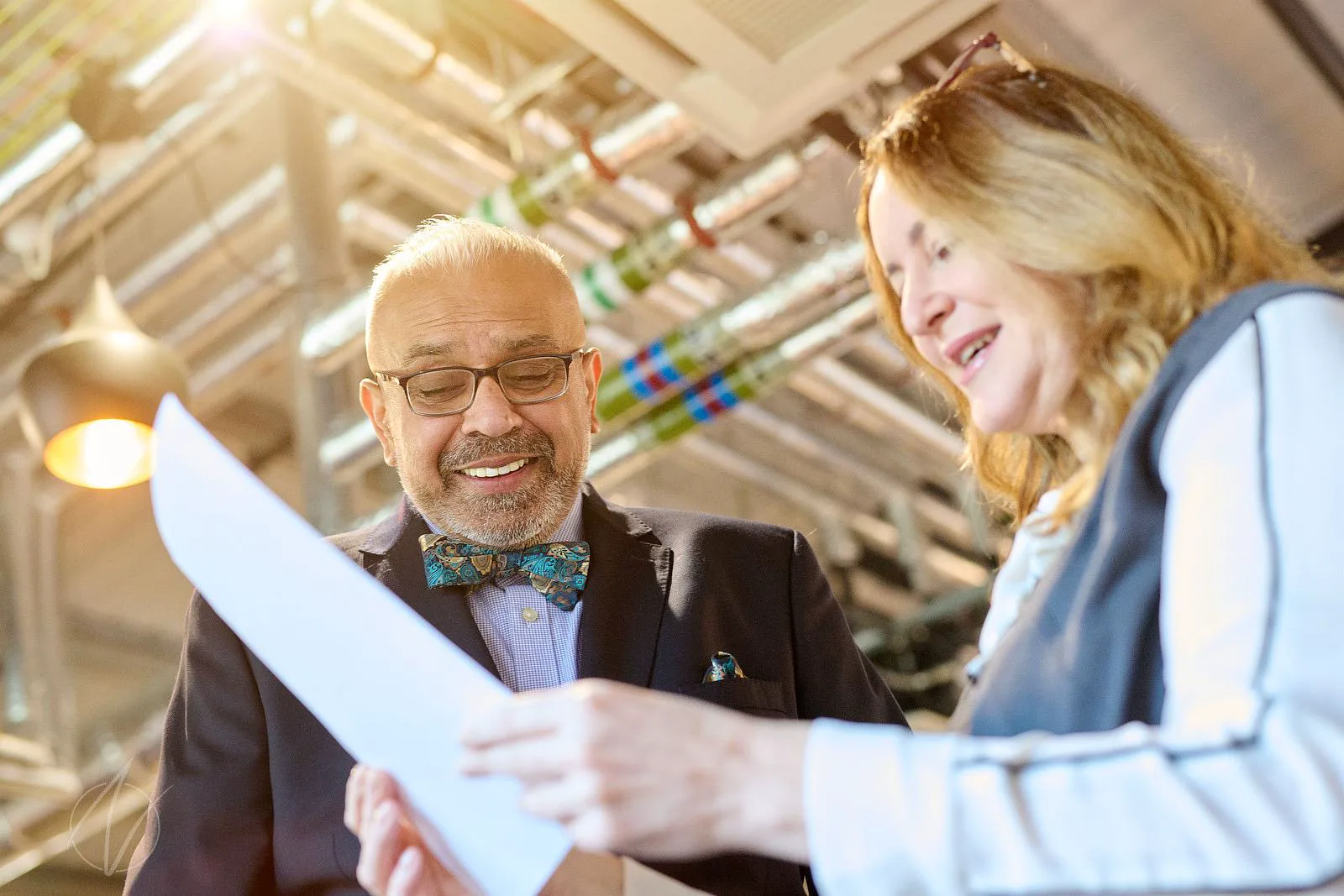 Speaker in bow tie and glasses reviewing notes with a colleague before going on stage