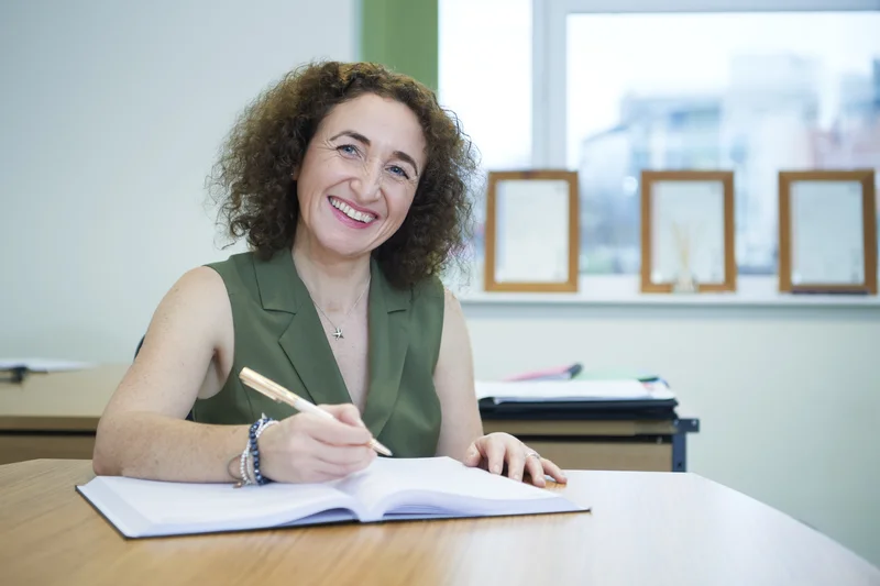 Lizzie Butler at her desk with a notebook, looking up with a warm and engaged expression
