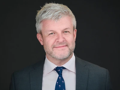 Classic professional headshot with warm expression and studio lighting on a dark background