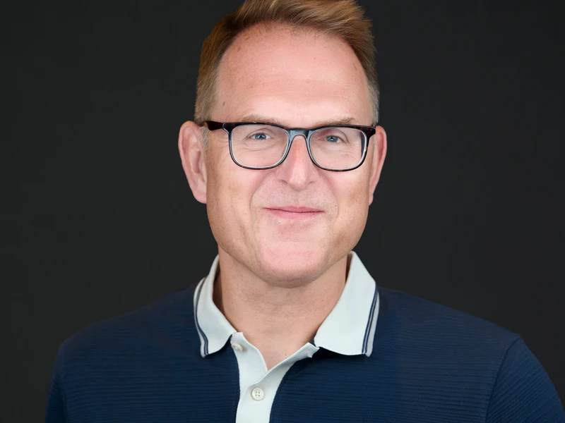 Corporate headshot of a man with glasses in a navy polo on a dark background