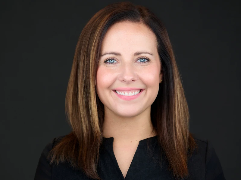 Professional corporate headshot of a woman in a black top on a dark background