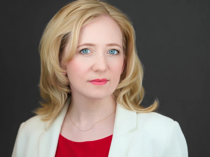 Professional business headshot of a woman in a white blazer on a dark background