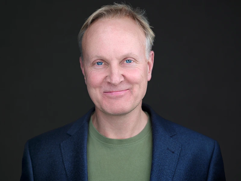 Professional business headshot of a man in a blazer on a dark background