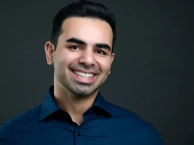 Professional headshot of a man with a confident, approachable expression on a dark background