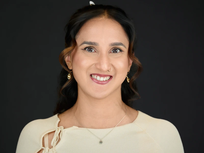 Studio headshot of a woman in a cream top on a dark background