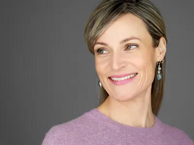 Executive woman in purple sweater with statement earrings, sophisticated side-glancing smile