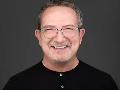 Professional man with glasses and grey goatee in black polo shirt, relaxed friendly expression