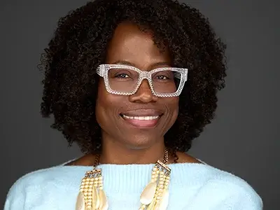 Confident Bristol professional with bold glasses, light blue top, layered necklace, natural curls, modern business portrait