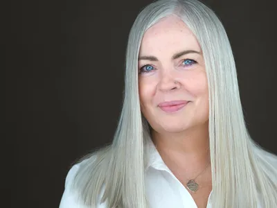 Corporate headshot of blonde executive woman with striking blue eyes wearing crisp white shirt, demonstrating polished professional style for corporate team photography
