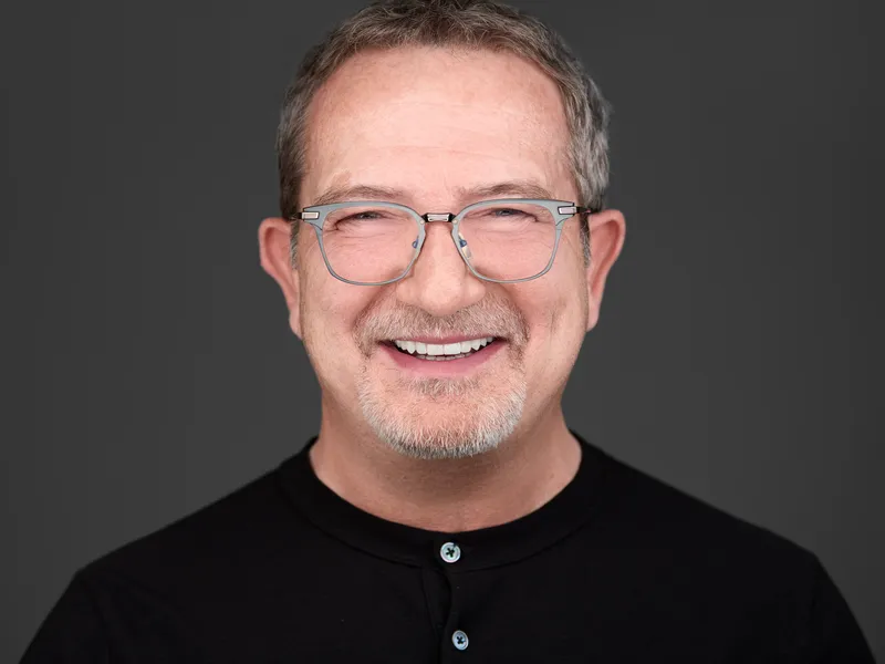 Professional man with glasses and grey goatee in black polo shirt, friendly approachable business portrait