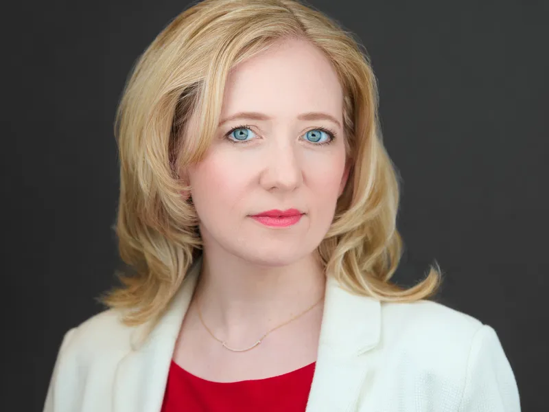 Professional blonde woman in white blazer over red top, polished executive business portrait