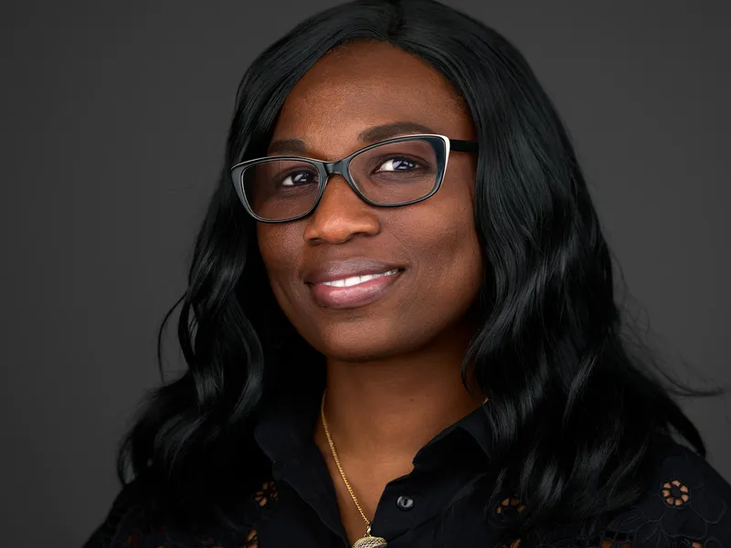 Professional woman with glasses and shoulder-length dark hair in black blouse, warm confident smile