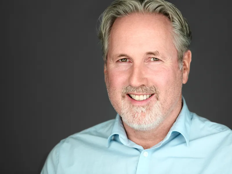 Senior executive with grey beard and styled hair in light blue shirt, warm experienced leadership presence