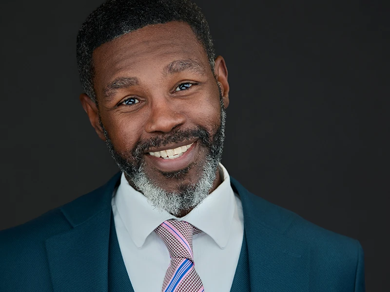 Confident professional with bold glasses, light blue top, layered necklace, natural curls, modern business portrait