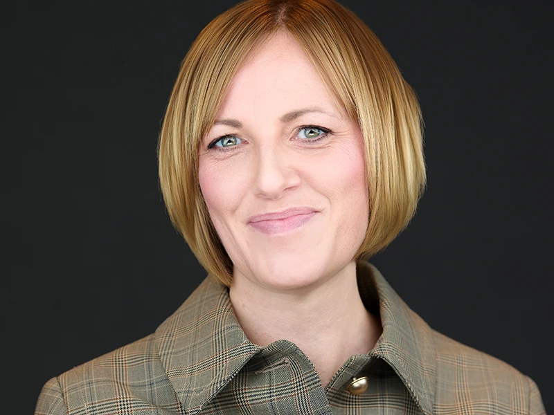 Professional portrait with dark background, business attire, warm smile, contemporary corporate headshot style