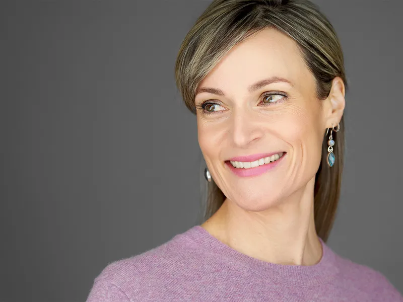 Professional woman in mauve sweater with statement earrings, natural smile against grey background