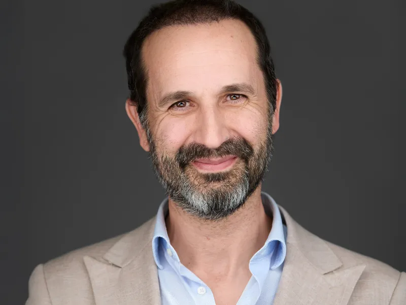 Mature professional with beard in light blazer and blue shirt, approachable executive headshot