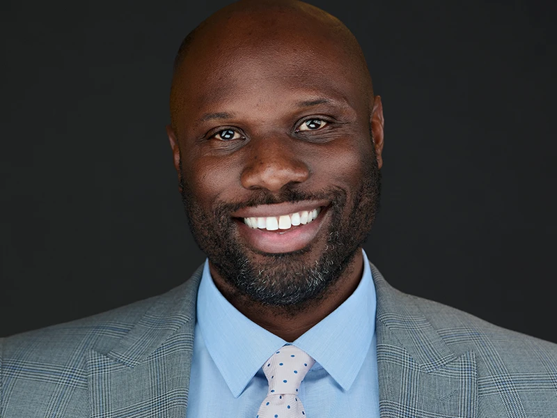 Executive headshot of a smiling man in a light grey suit and blue shirt, photographed by proheadshots.mom.