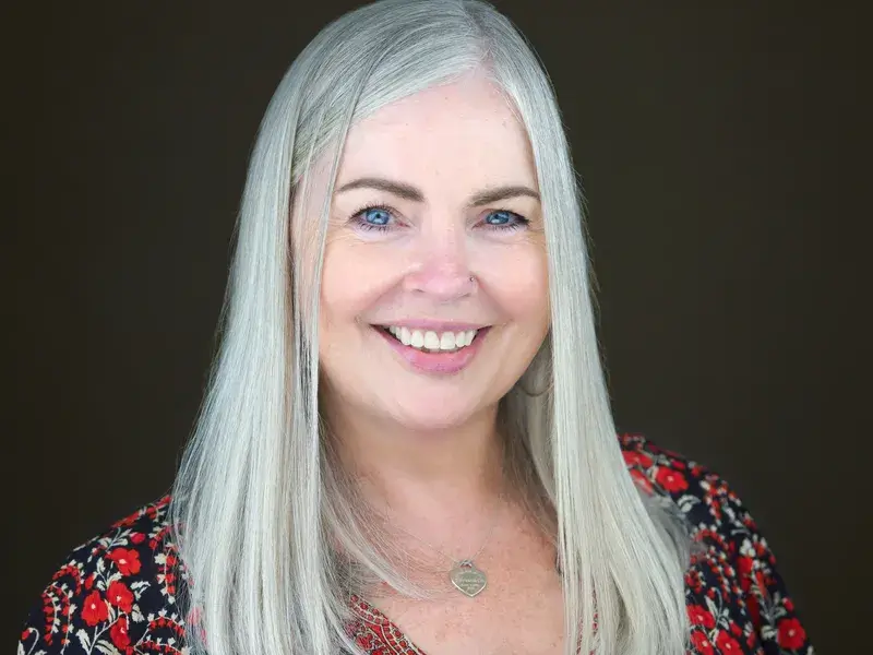 Professional woman with long blonde hair in red and black floral dress, radiating warmth with bright genuine smile showing personality-driven business portrait
