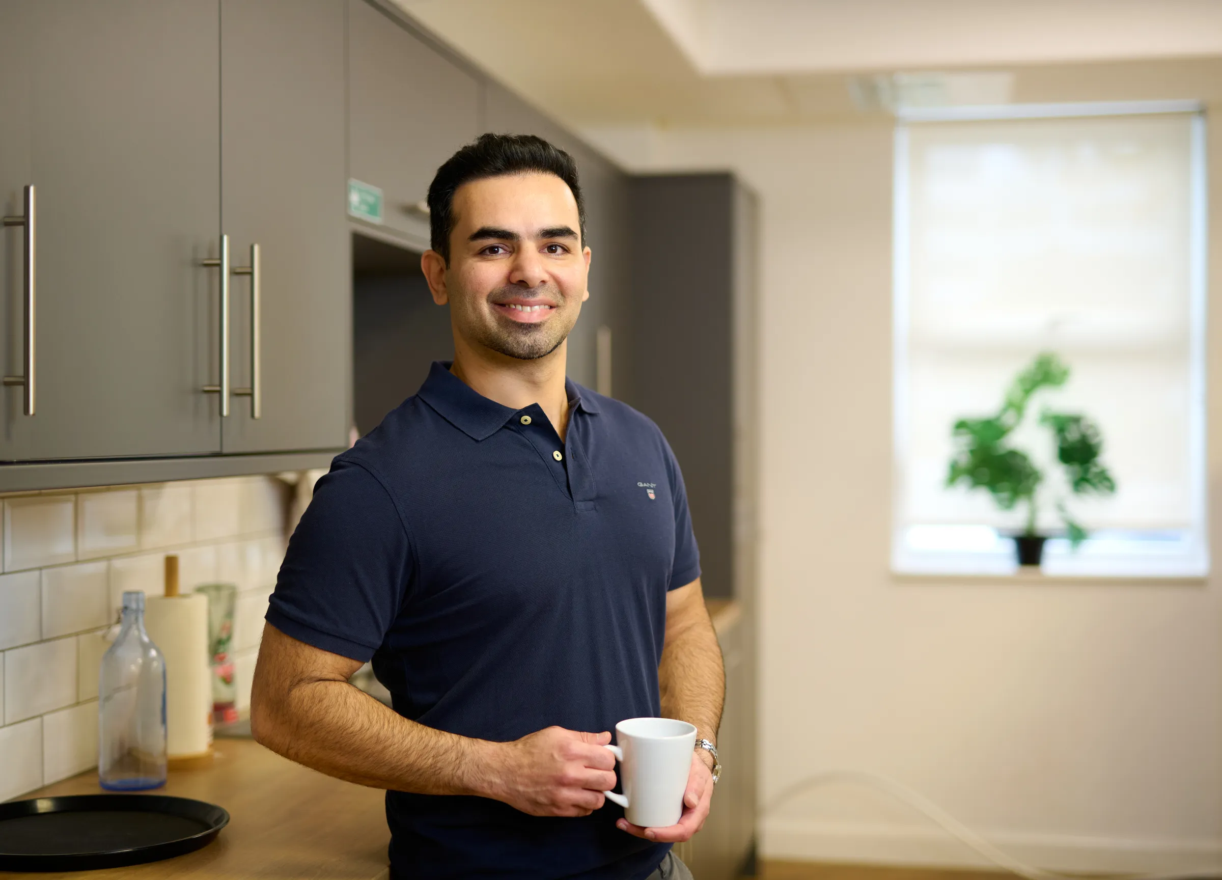 Ben Rahmani standing in the kitchen area holding a mug, relaxed and approachable