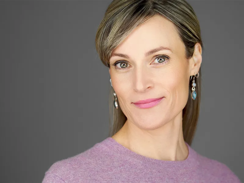 Professional woman with styled blonde hair wearing purple sweater and statement earrings, sophisticated portrait