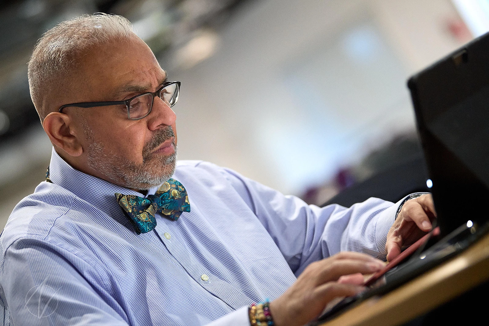 A distinguished professional in a light blue shirt and patterned bow tie concentrates while working, his thoughtful expression and stylish accessories creating a portrait of focused expertise.