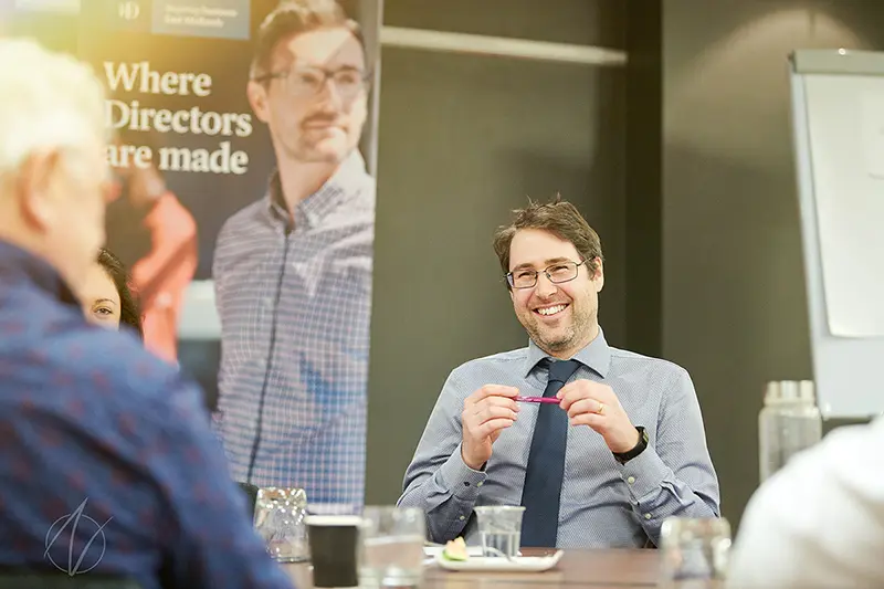 A smiling director participates in a boardroom discussion, showing genuine engagement with colleagues during a professional development session.
