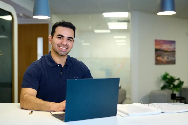 Ben Rahmani, MedStride founder, smiling at his laptop in a modern Bournemouth office