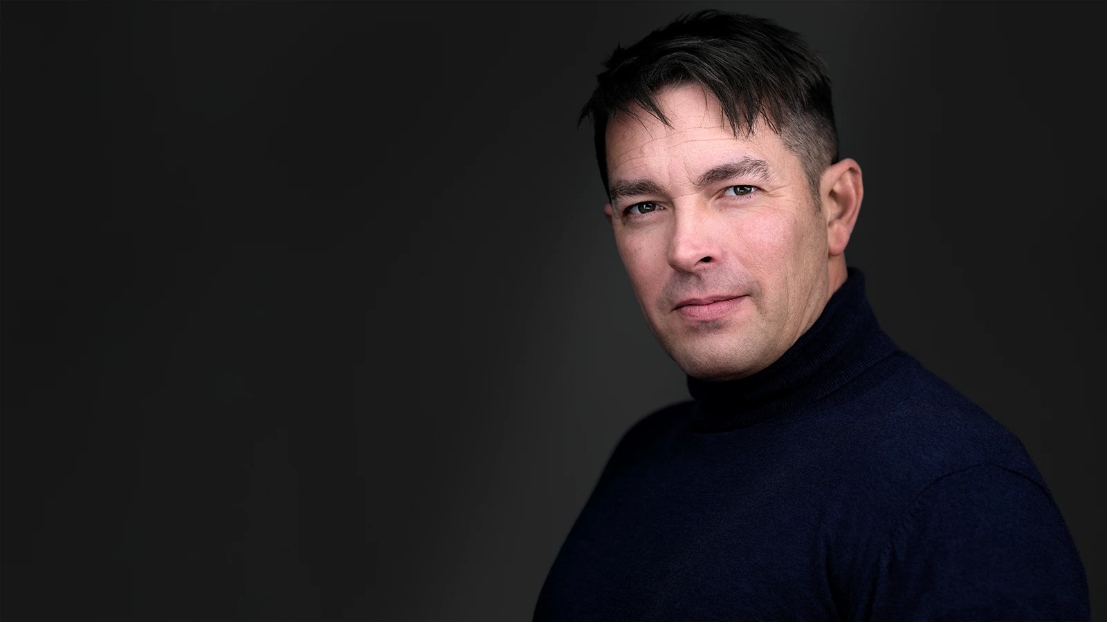 Personal branding portrait: man in a black turtleneck, studio-lit, direct confident gaze