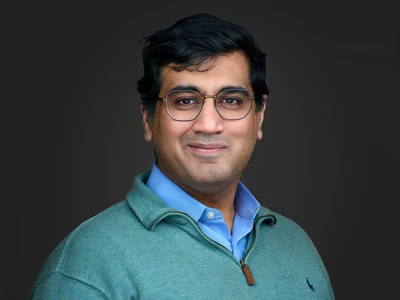 Man in jumper with glasses, thoughtful expression, dark background