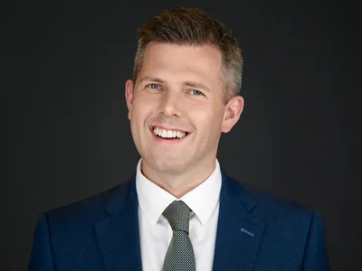 Man in a dark suit with a direct, assured gaze for his professional headshot