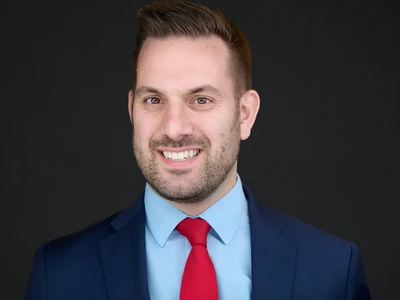 Bearded man in a well-fitted suit with a composed, natural expression in a corporate headshot