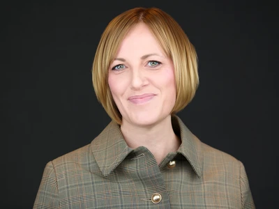 Woman in a dark grey blazer, warm natural expression, studio-lit portrait