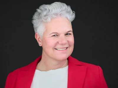 A woman in a charcoal blazer, engaged and professional expression