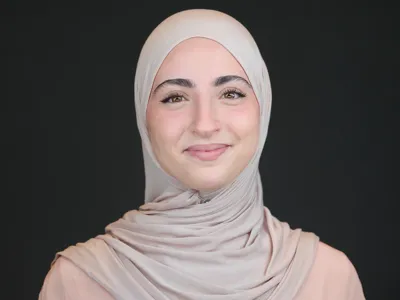 Professional woman in a hijab with a calm, assured expression against a dark grey background