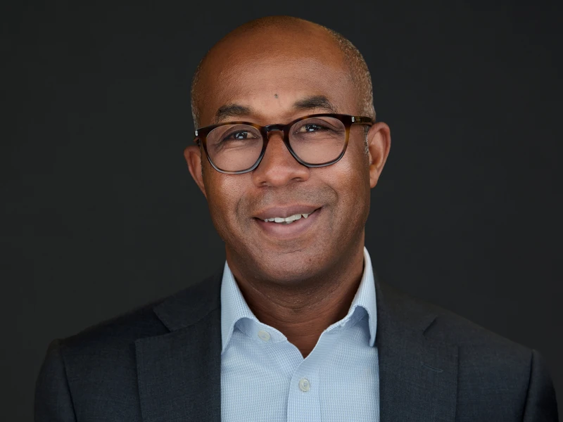 Man in glasses and a blazer, open-collar shirt and a calm, assured look to camera