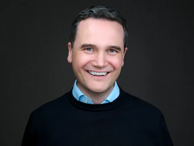 Headshot of a man in a dark grey jumper on a dark studio background