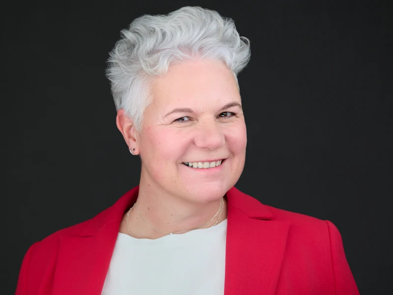 Woman in a blazer, composed direct eye contact, professional headshot