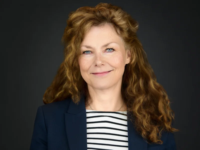 Studio headshot of a woman with red hair in a dark grey blazer, natural expression